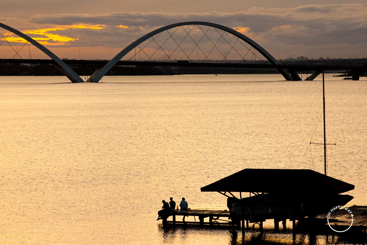 Fotos de silhueta: três amigos em pier no Lago Paranoá, em Brasília, com a ponte JK ao fundo.