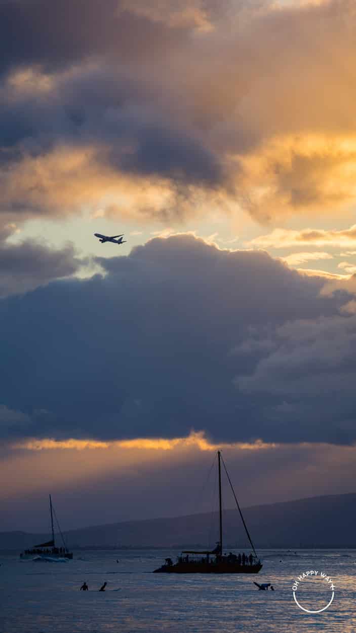 Avião, barcos e surfistas no pôr do sol em Waikiki, Honolulu, Havaí.