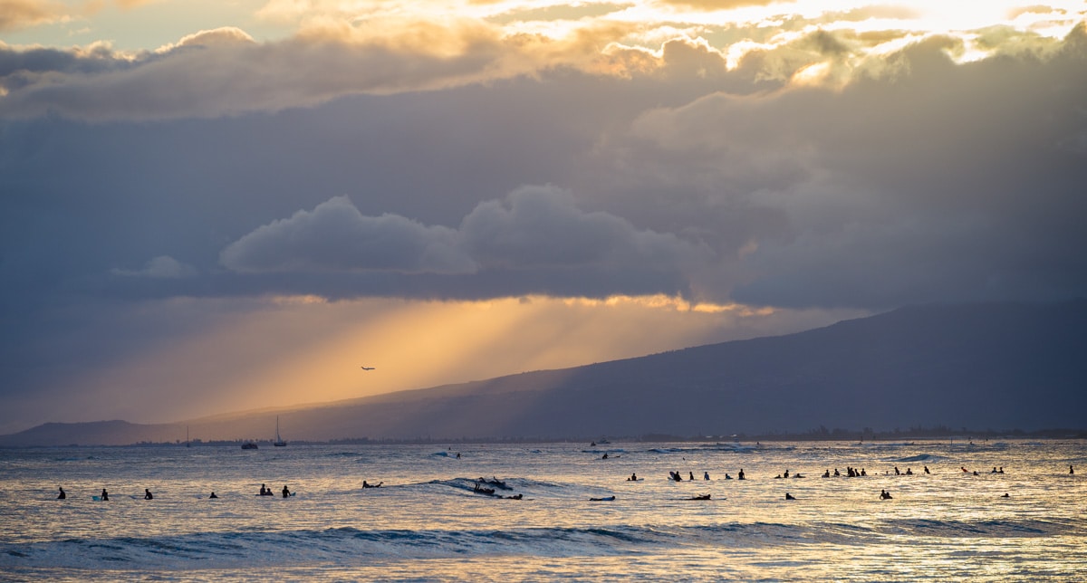 Pôr do sol no Hawaii: Surfistas, raios de sol e avião na praia de Waikiki, em Honolulu.