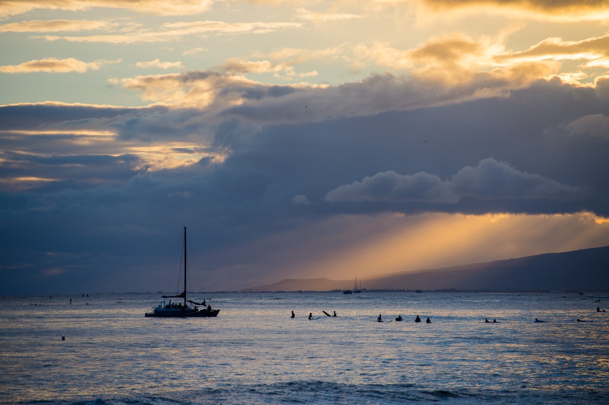 Pôr do sol no Hawaii: Surfistas, raios de sol e barco na praia de Waikiki, em Honolulu.