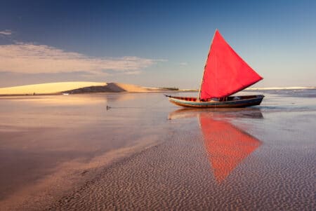 Barco com vela vermelha e a duna do Pôr do Sol na praia de Jericoacoara, no Ceará.