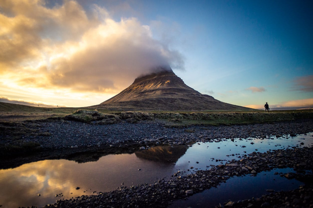 Homem andando em frente à montanha Kirkjufell na península Snæfellsnes, na Islândia.